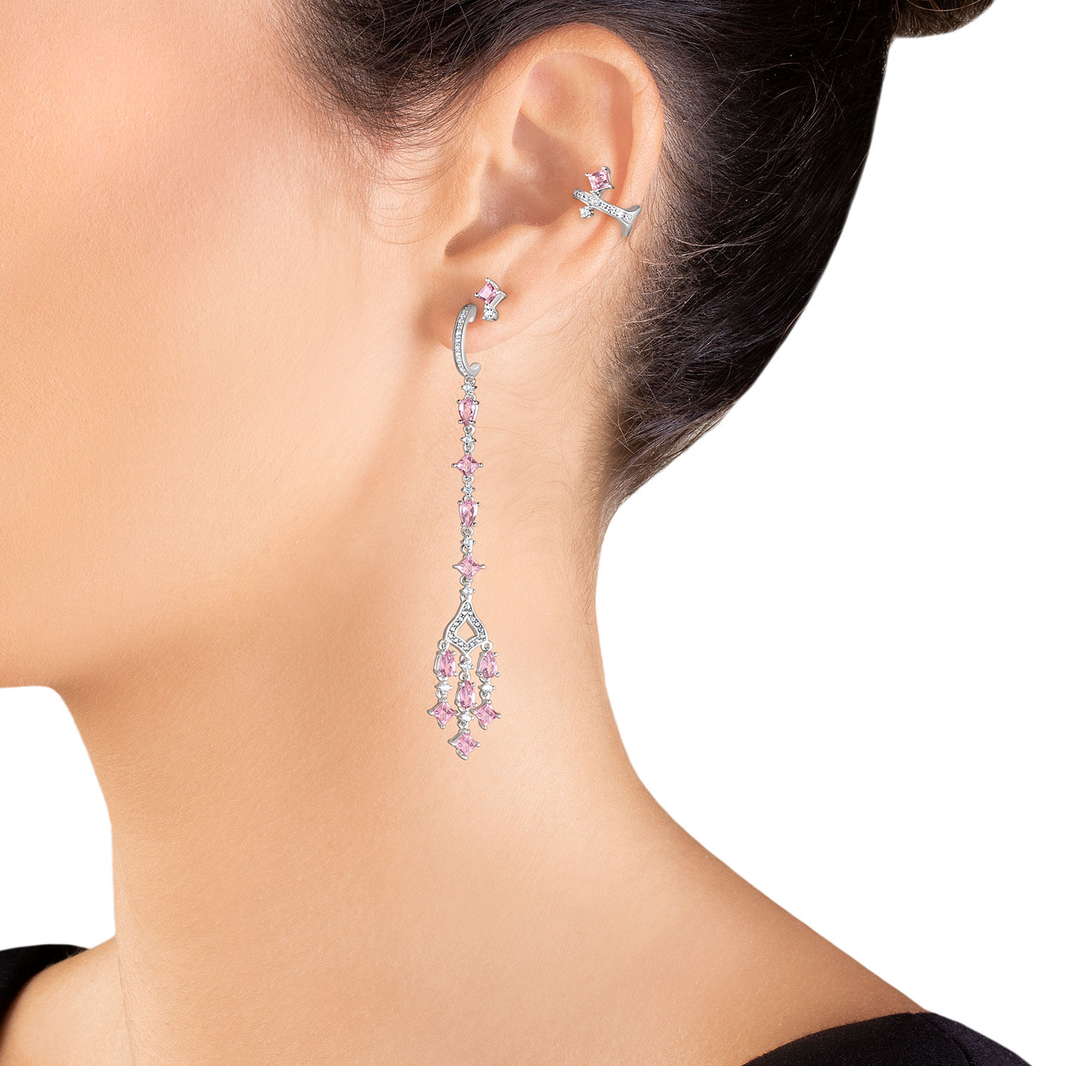 Brinco longo de prata com pedra rosa e detalhes em zircônia, pendurado na orelha de uma mulher.