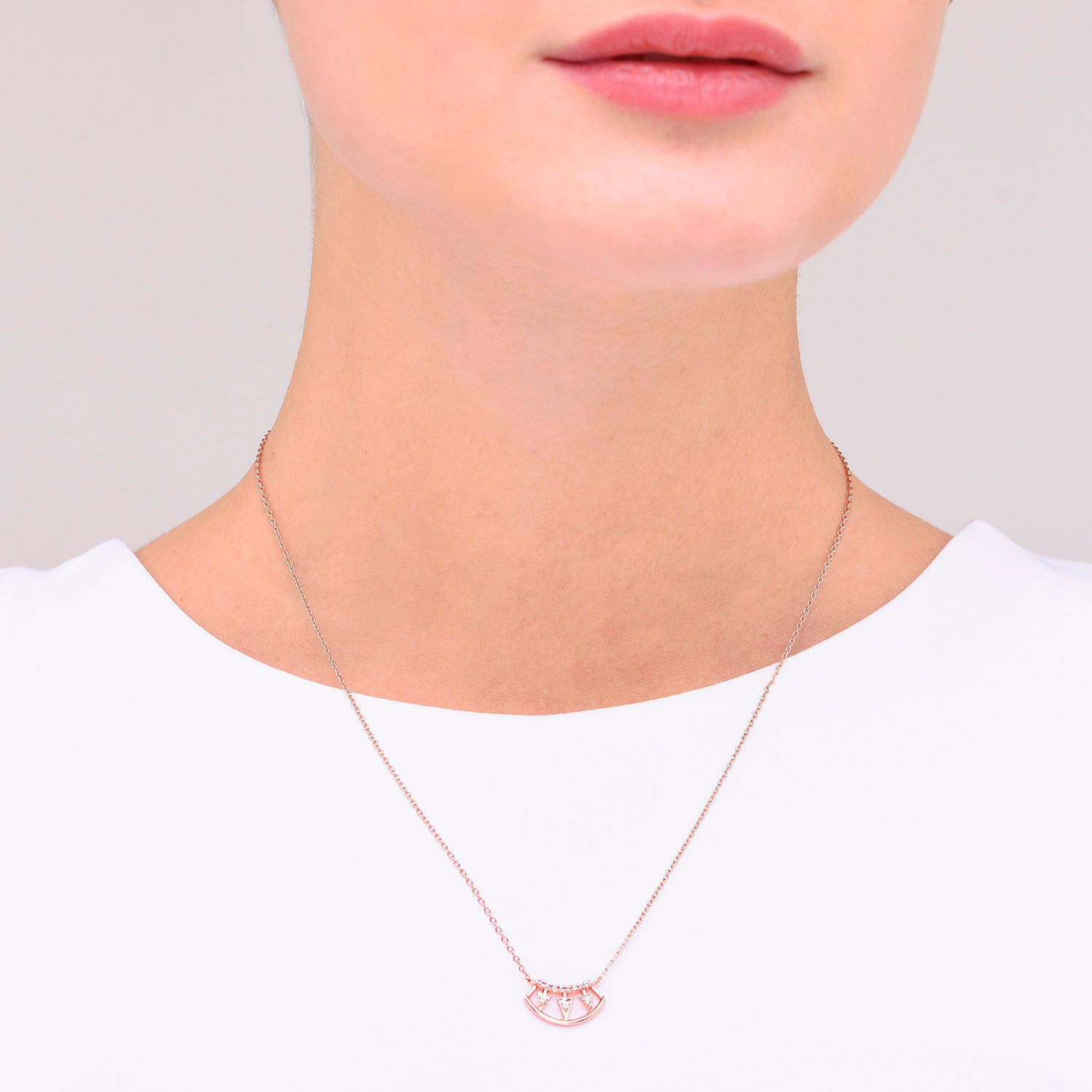 Colar delicado de corrente fina com pingente em forma de arco com detalhes em pedras, usado por uma pessoa com pele clara e roupa branca.