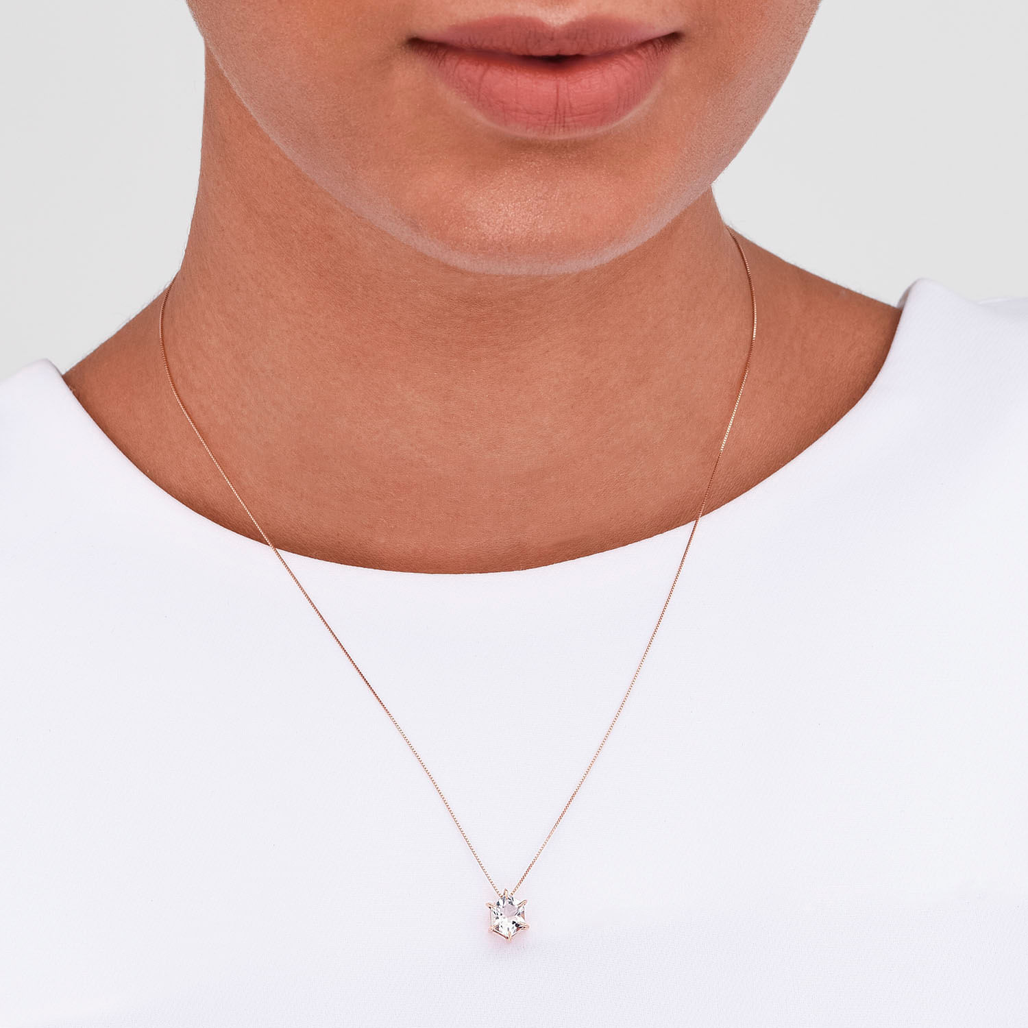 Colar delicado com pingente de pedra brilhante, usado por uma pessoa com pele morena clara e camiseta branca.