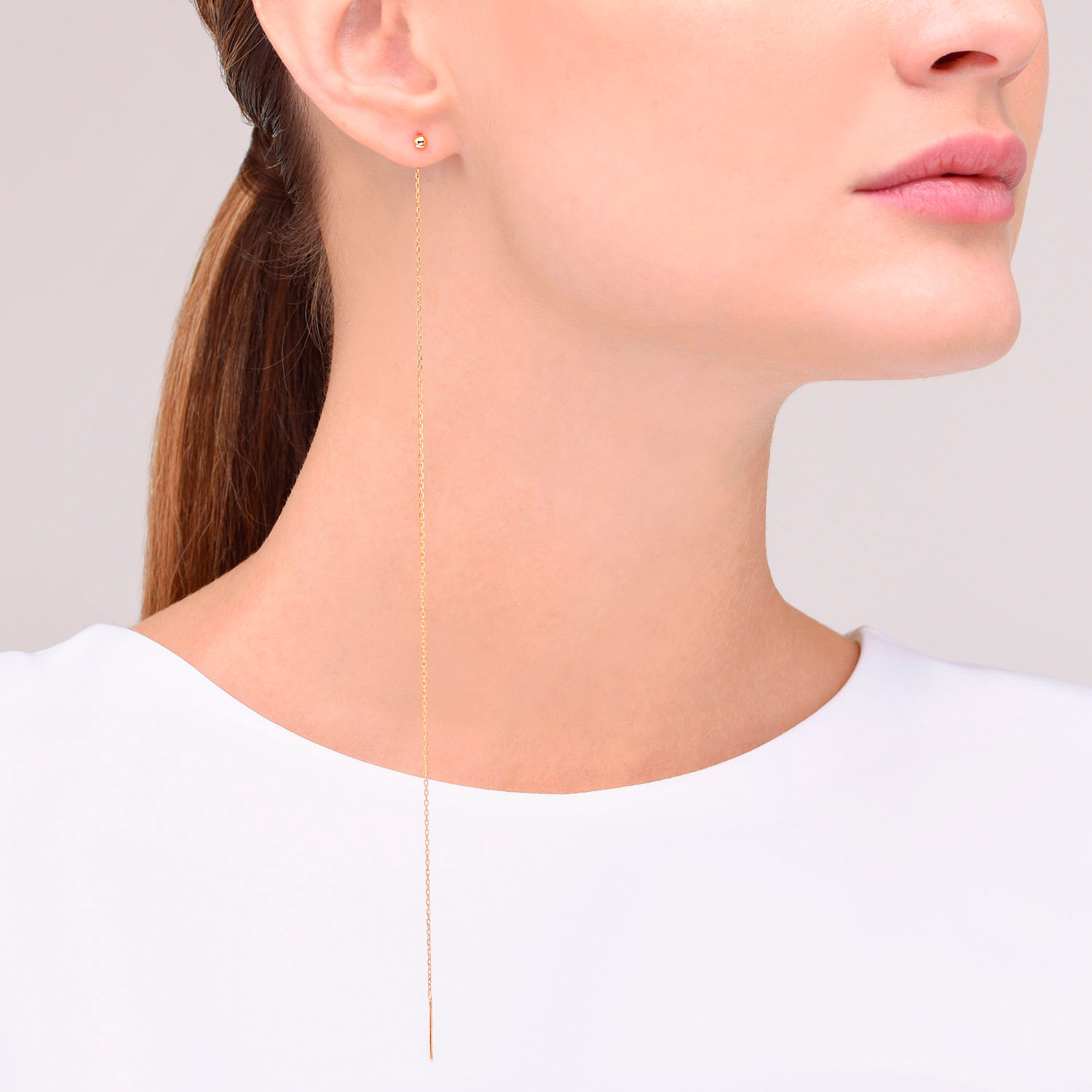 Close-up de uma mulher com o cabelo puxado para trás, usando brincos pequenos e uma corrente dourada longa no pescoço.