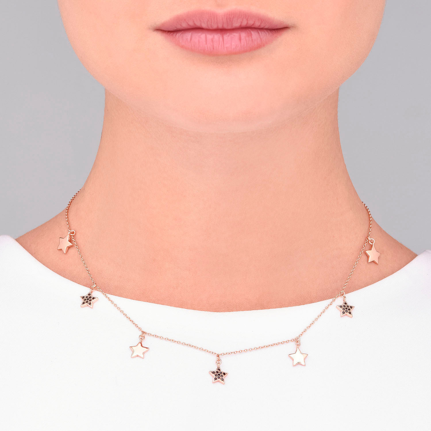 Colar dourado com pingentes de estrelas, alguns com detalhes em preto, usado no pescoço de uma pessoa.