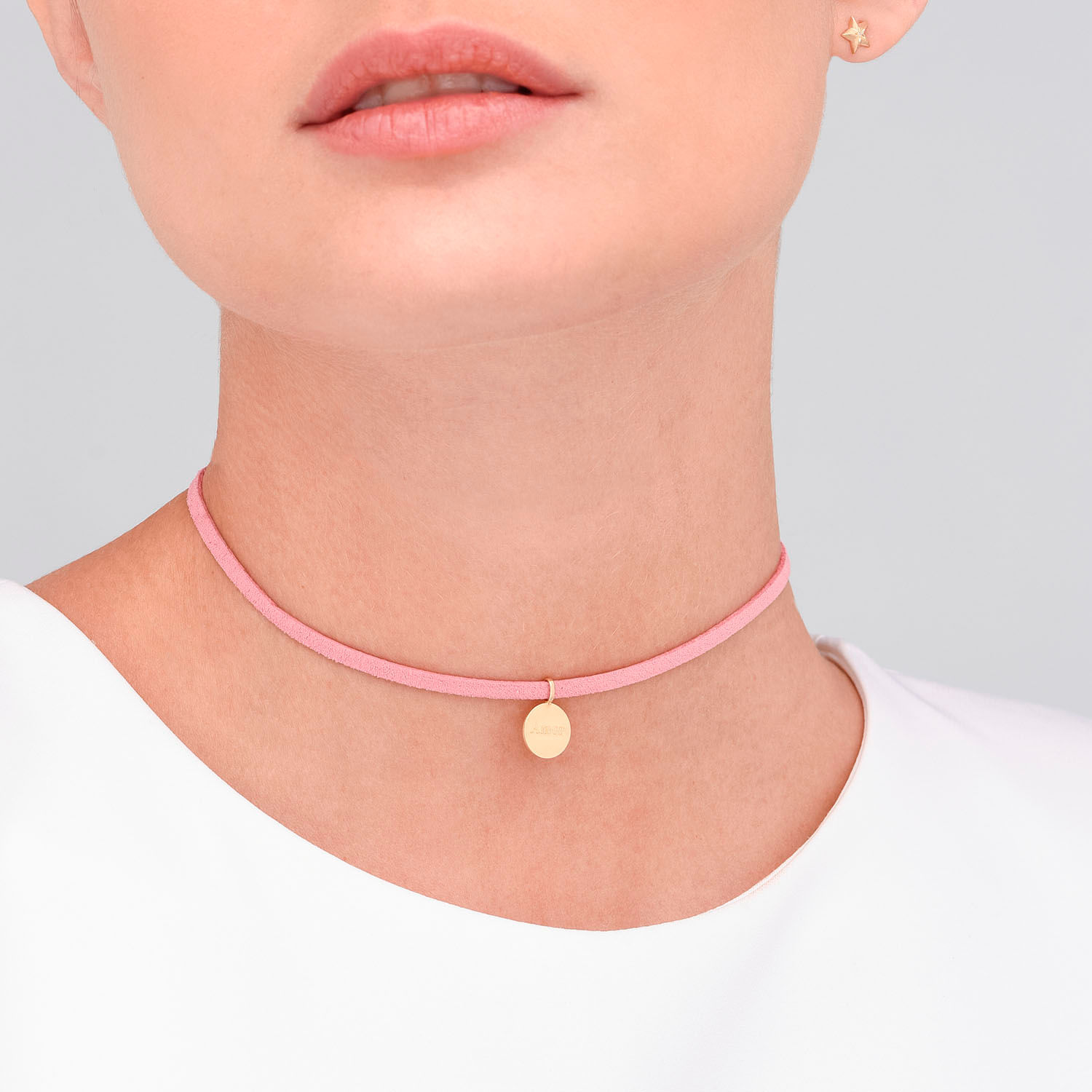 Colar fino rosa com pingente dourado circular, usado por uma pessoa com pele clara e cabelo castanho claro.
