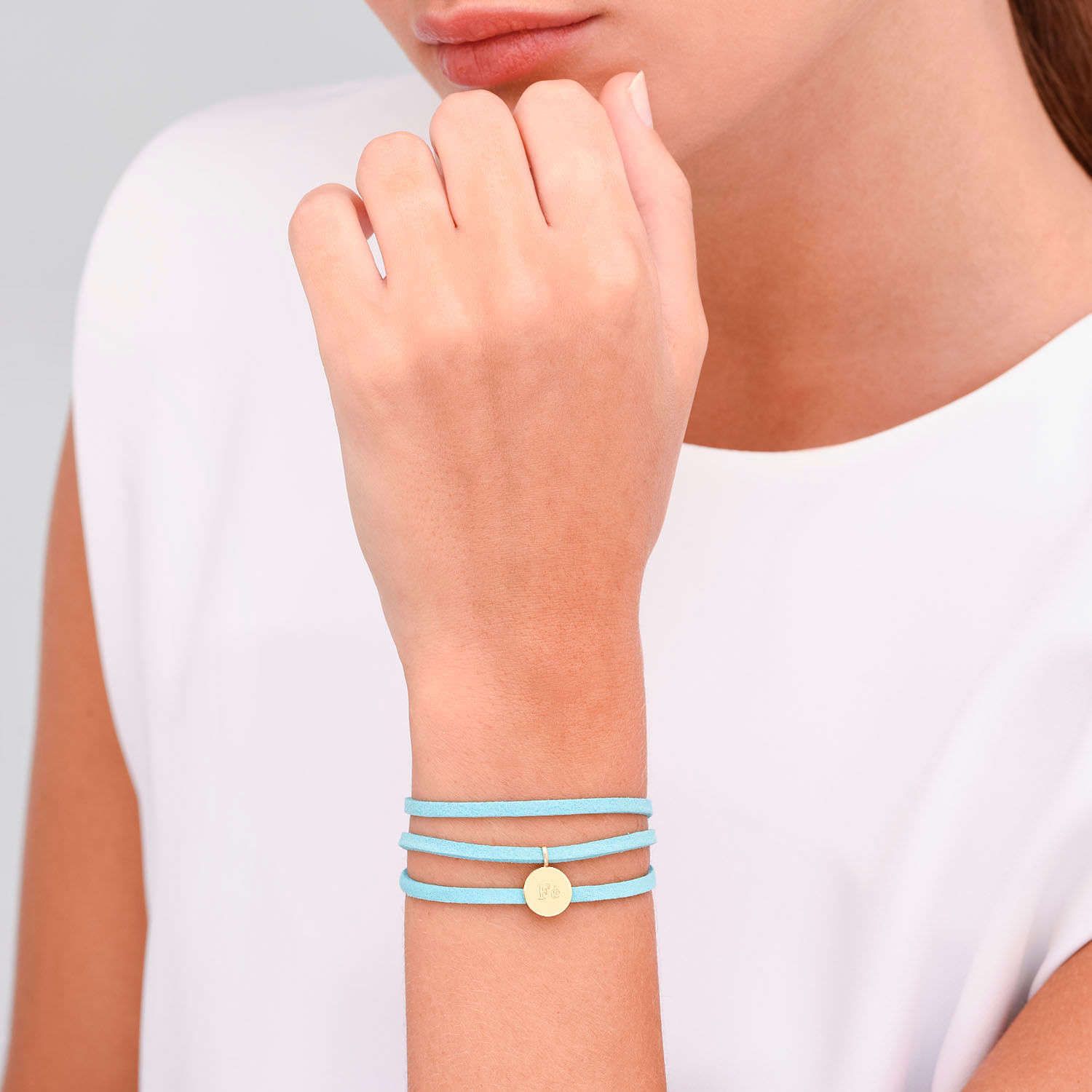 Mulher usando quatro pulseiras finas azul claro com um pingente dourado no pulso esquerdo, vestindo blusa branca.