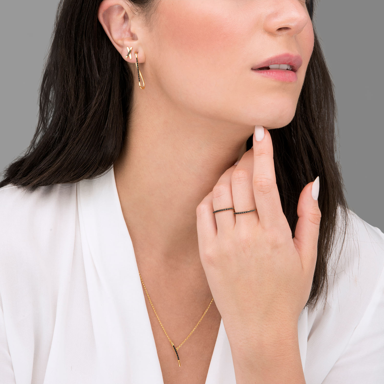 Mulher com brincos dourados, vestido branco, usando um colar dourado e uma aliança delicada na mão esquerda.