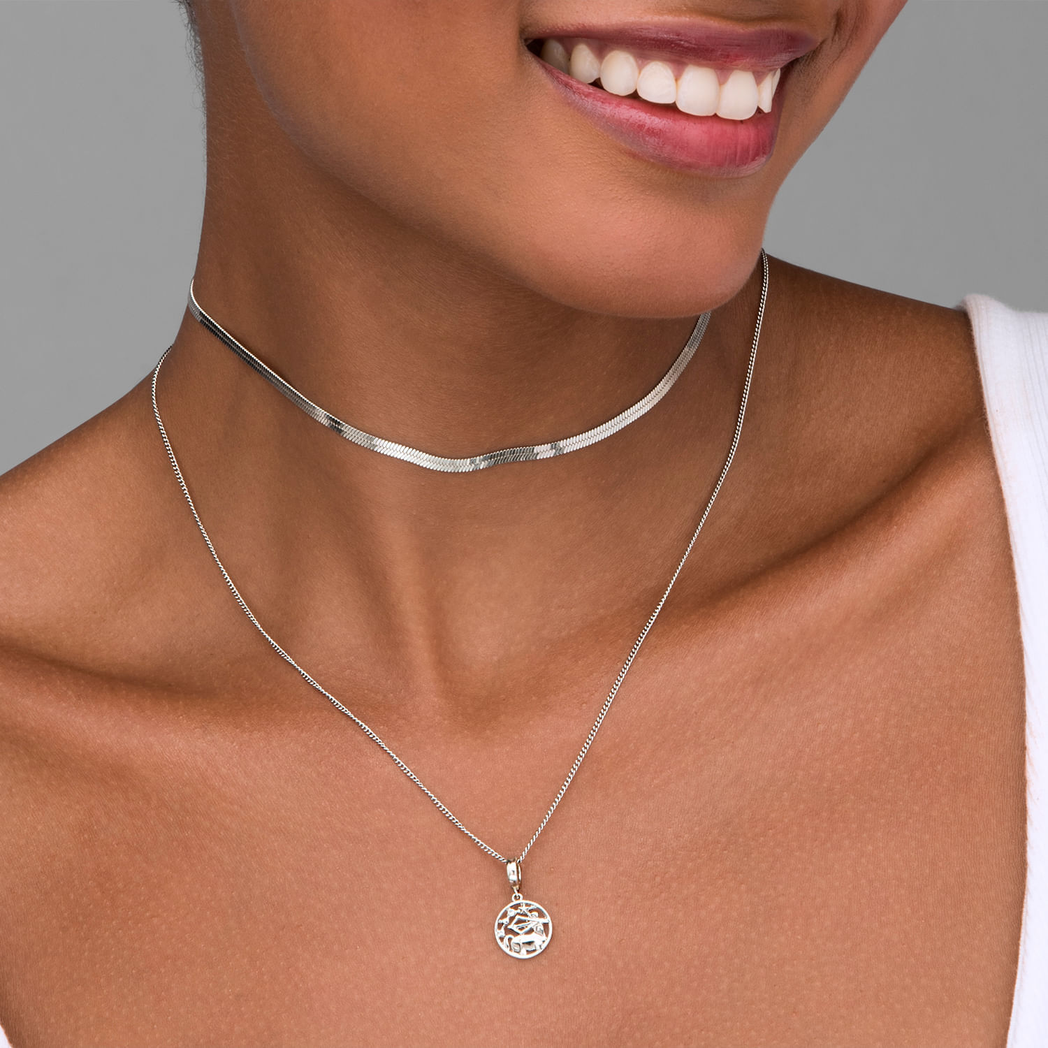 Mulher usando três colares de prata, incluindo um choker e um com pingente circular com árvore da vida.