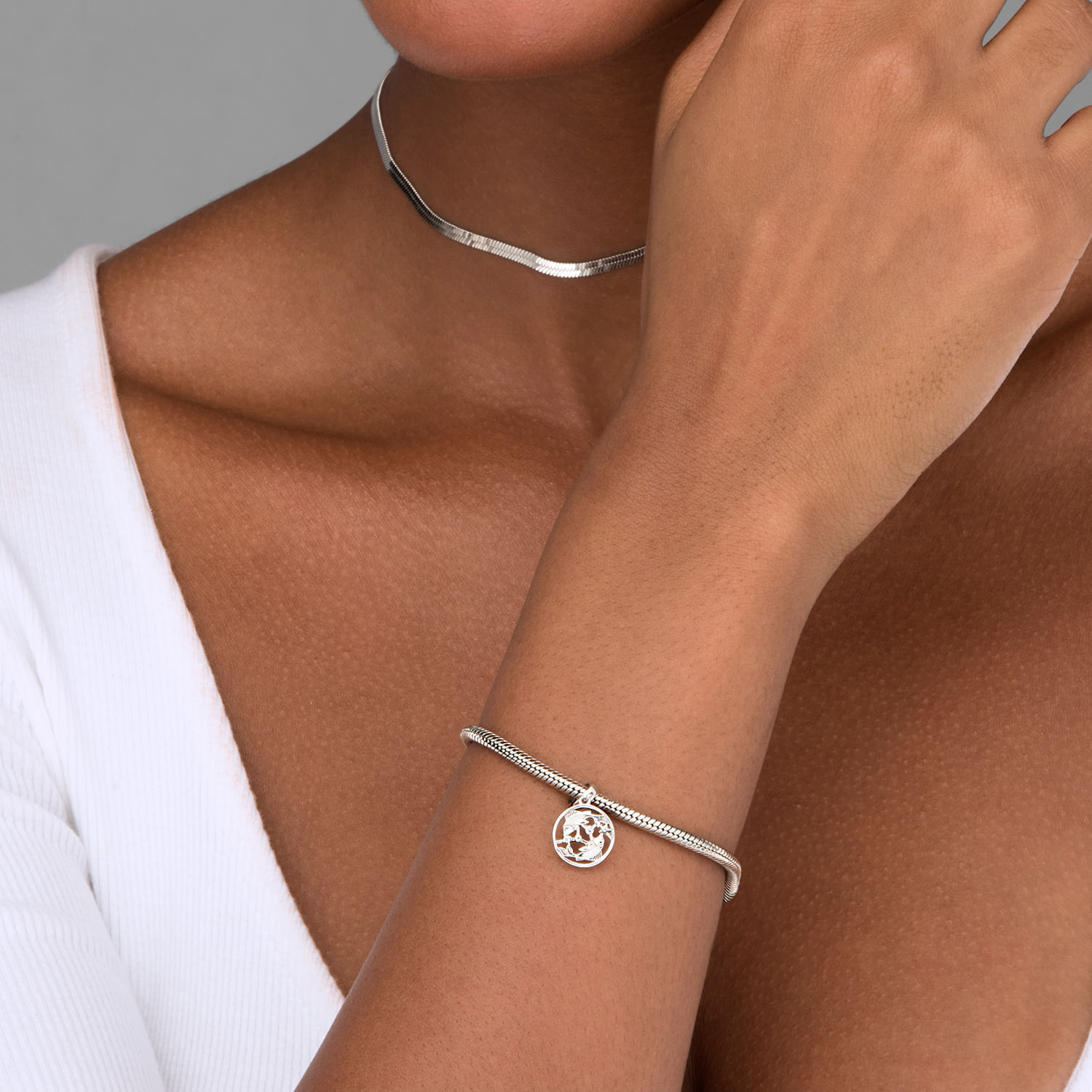 Pulsera de prata com pingente de árvore, acompanhada por um colar de prata simples, usada por uma mulher com tom de pele morena clara.