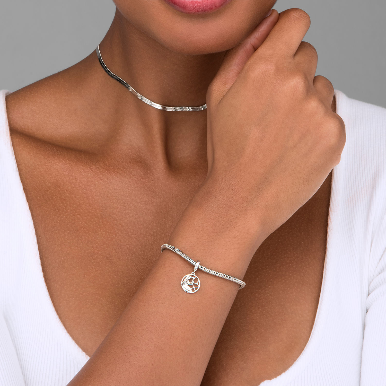 Mulher usando colar e pulseira prateados, com símbolo de árvore na pulseira.