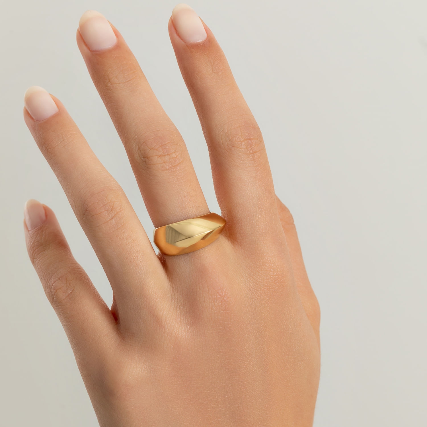 Mão com unhas naturais usando uma aliança dourada lisa e brilhante no dedo médio.