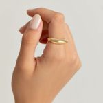 Dedo com unha bem cuidada usando um anel dourado em forma de meia lua na parede branca.