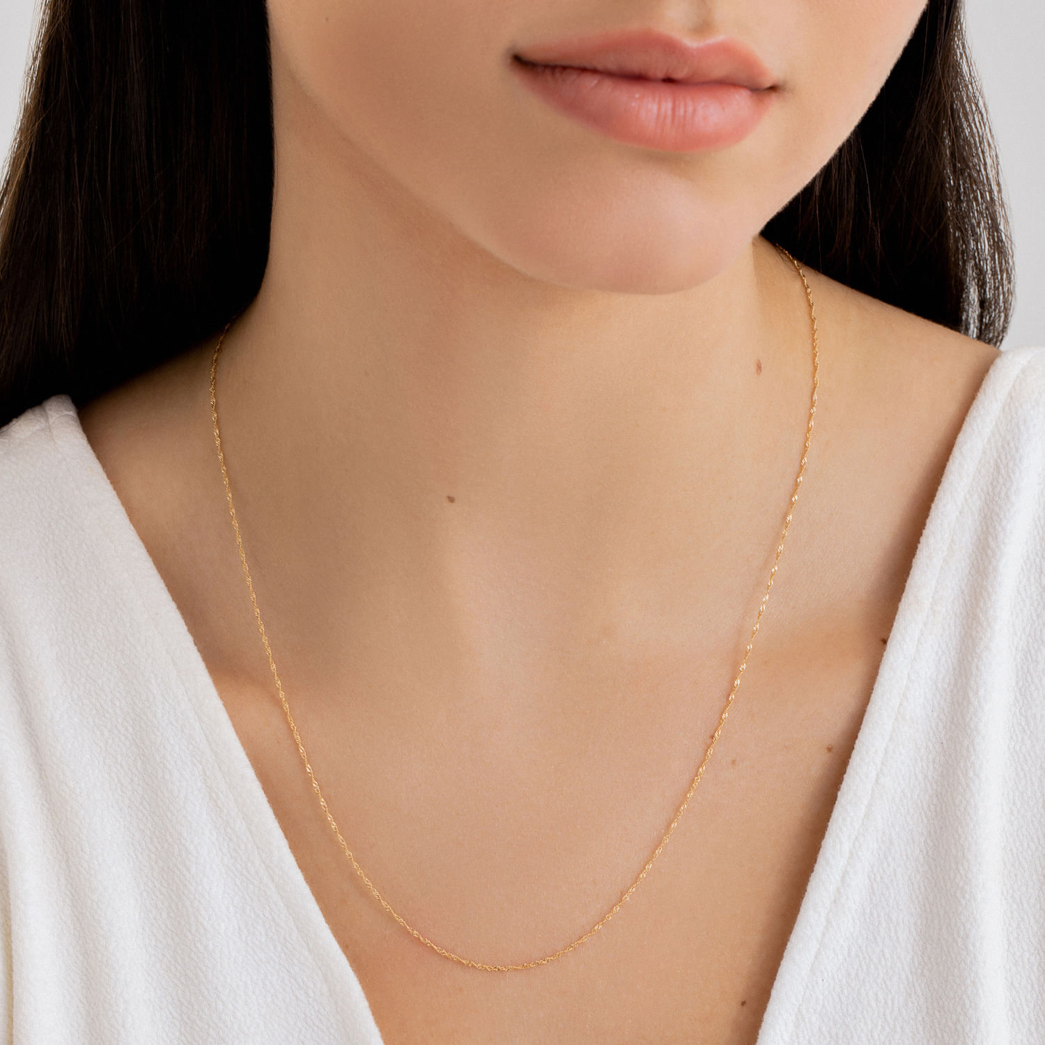 Colar delicado dourado em volta do pescoço de uma mulher com pele clara, usando roupa branca.