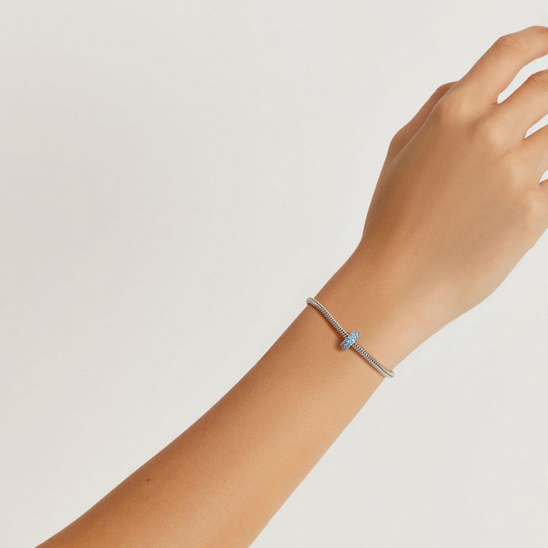 Pulseira de corrente fina com pingente em formato de cruz com pequenos detalhes azuis.