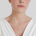 Mulher com colar e pingente de ouro com pedras verdes, vestida com blusa branca e acessórios de orelha.