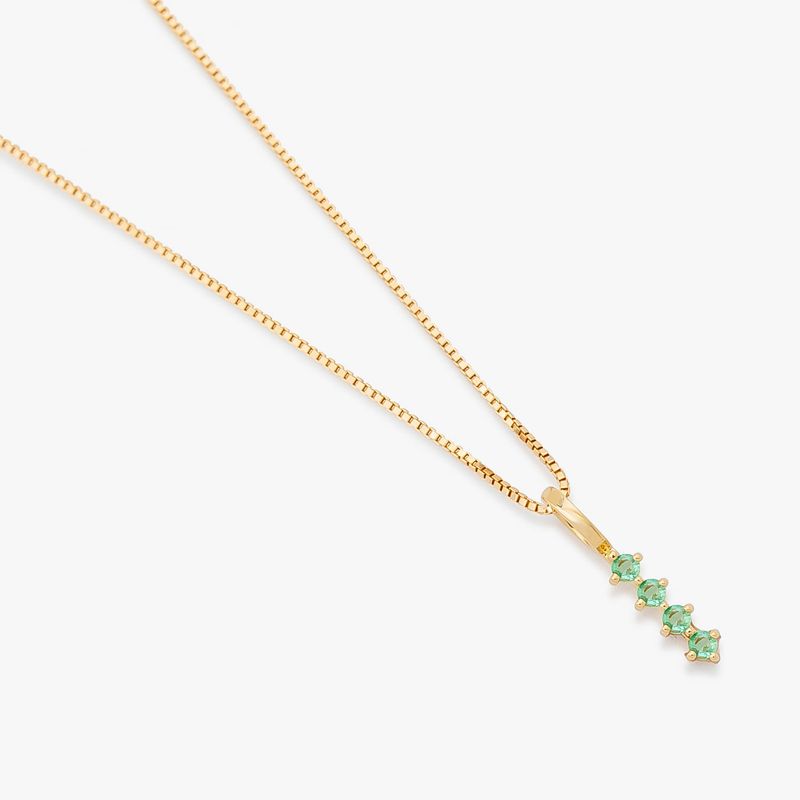 Colar com pingente de ouro com cinco pedras verdes em destaque, em um fundo branco.