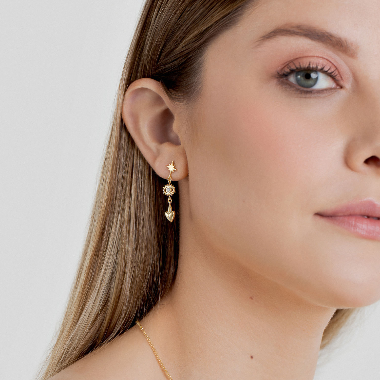 Piercing de orelha com múltiplos brincos dourados, incluindo uma estrela, um olho, uma estrela menor e um coração.