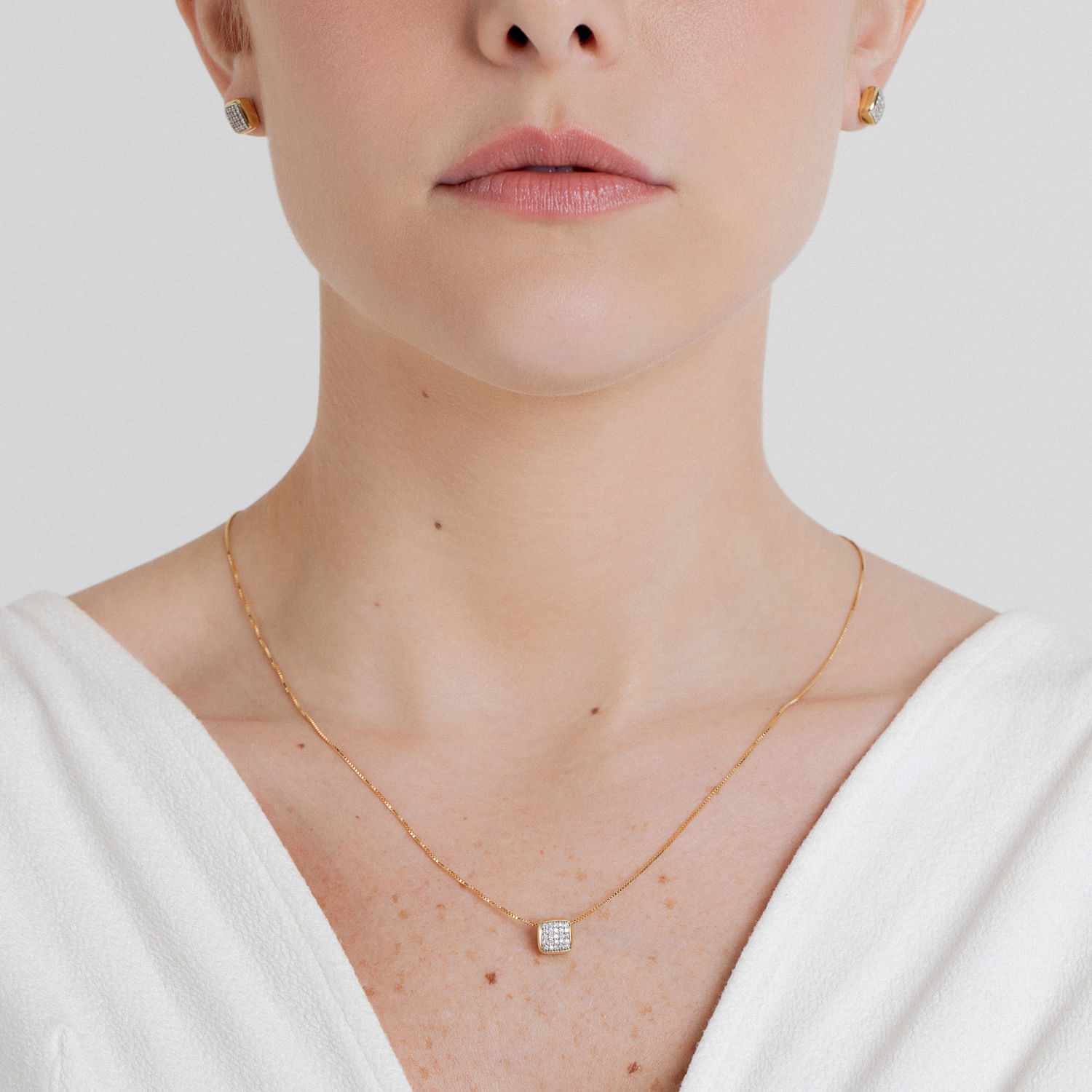 Close de uma mulher usando um colar de corrente de ouro com um pingente quadrado incrustado com pequenos diamantes.