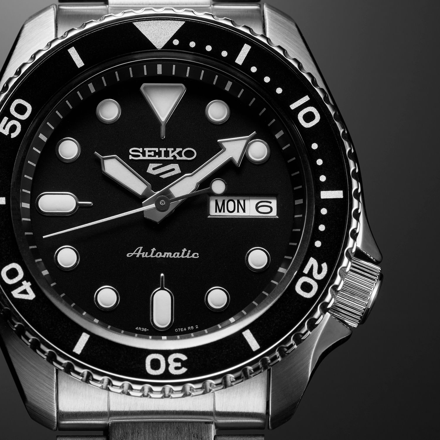 Relógio Seiko com mostrador preto, indicadores de hora em círculos e ponteiros prateados, vidro e bezel rotativos, e bracelete metálico.
