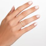 Mão com unhas claras e bem cuidadas usando um anel dourado delicado na finger. Fundo branco liso.