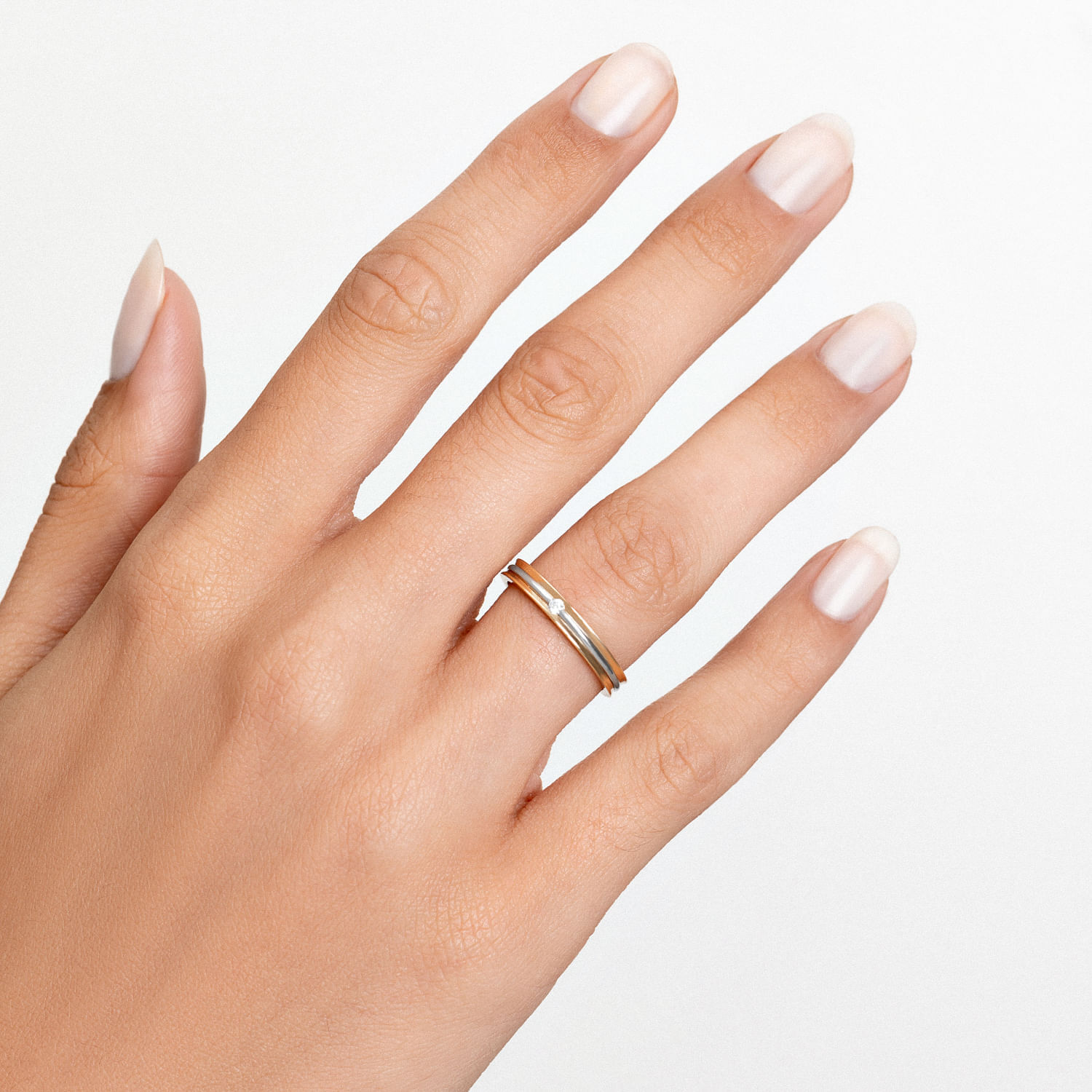 Dedo com unha esmaltada de cor nude usando um anel dourado simples com uma pedra pequena.