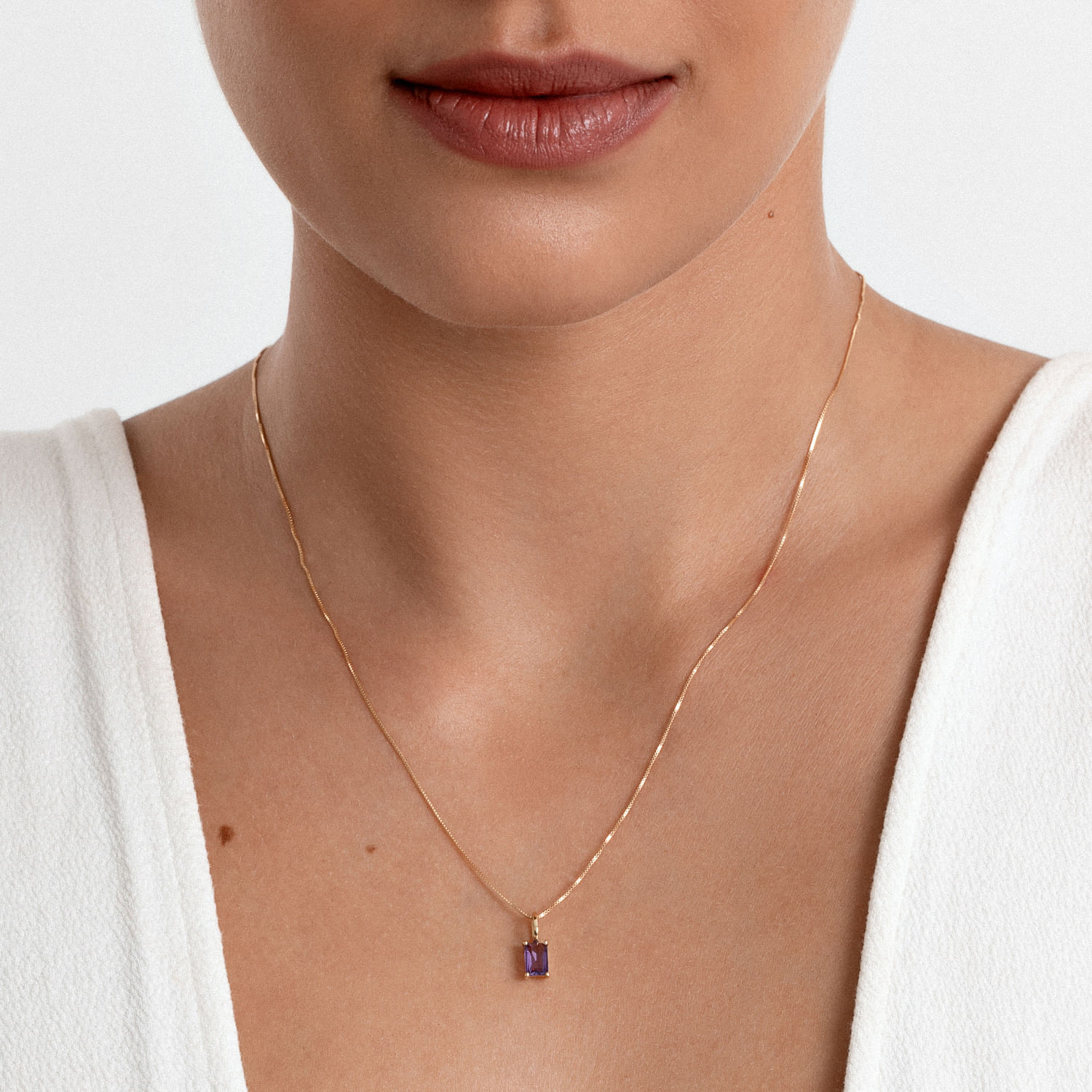 Colar dourado com pingente retangular roxo.