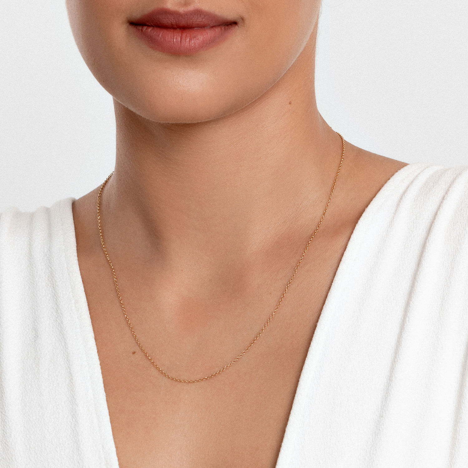 Colar delicado dourado com pequenas bolinhas, usado por uma mulher com blusa branca.