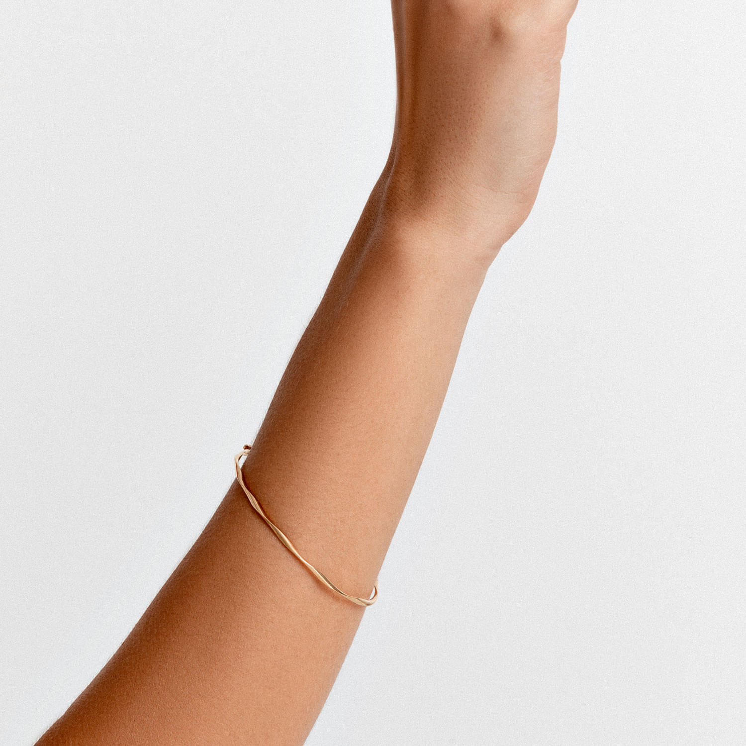 Mão de pessoa com pele morena, usando uma pulseira fina dourada, contra fundo branco.