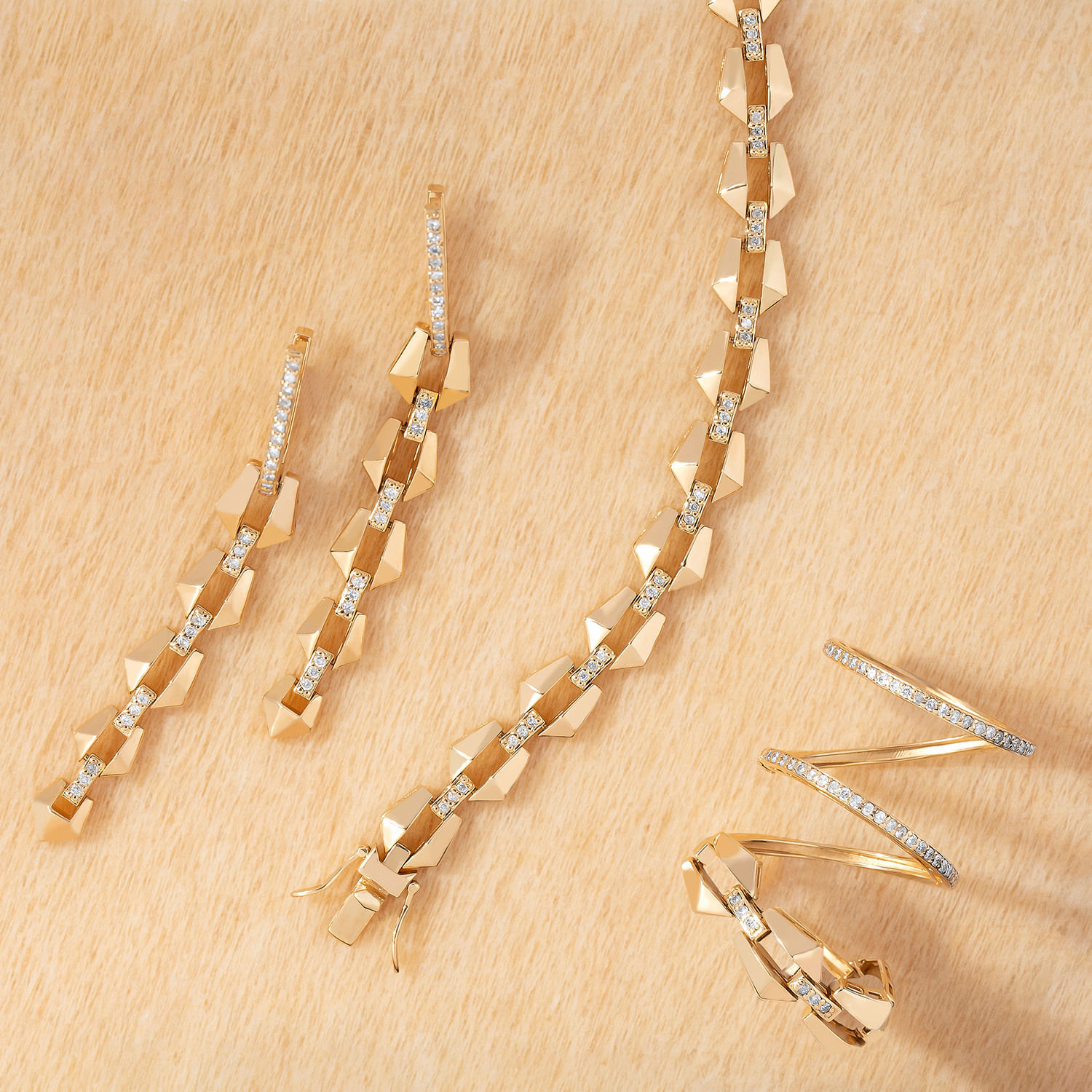 Conjunto de joias douradas com detalhes em zircônias, incluindo brincos longos, anel e duas peças semelhantes a grampos.