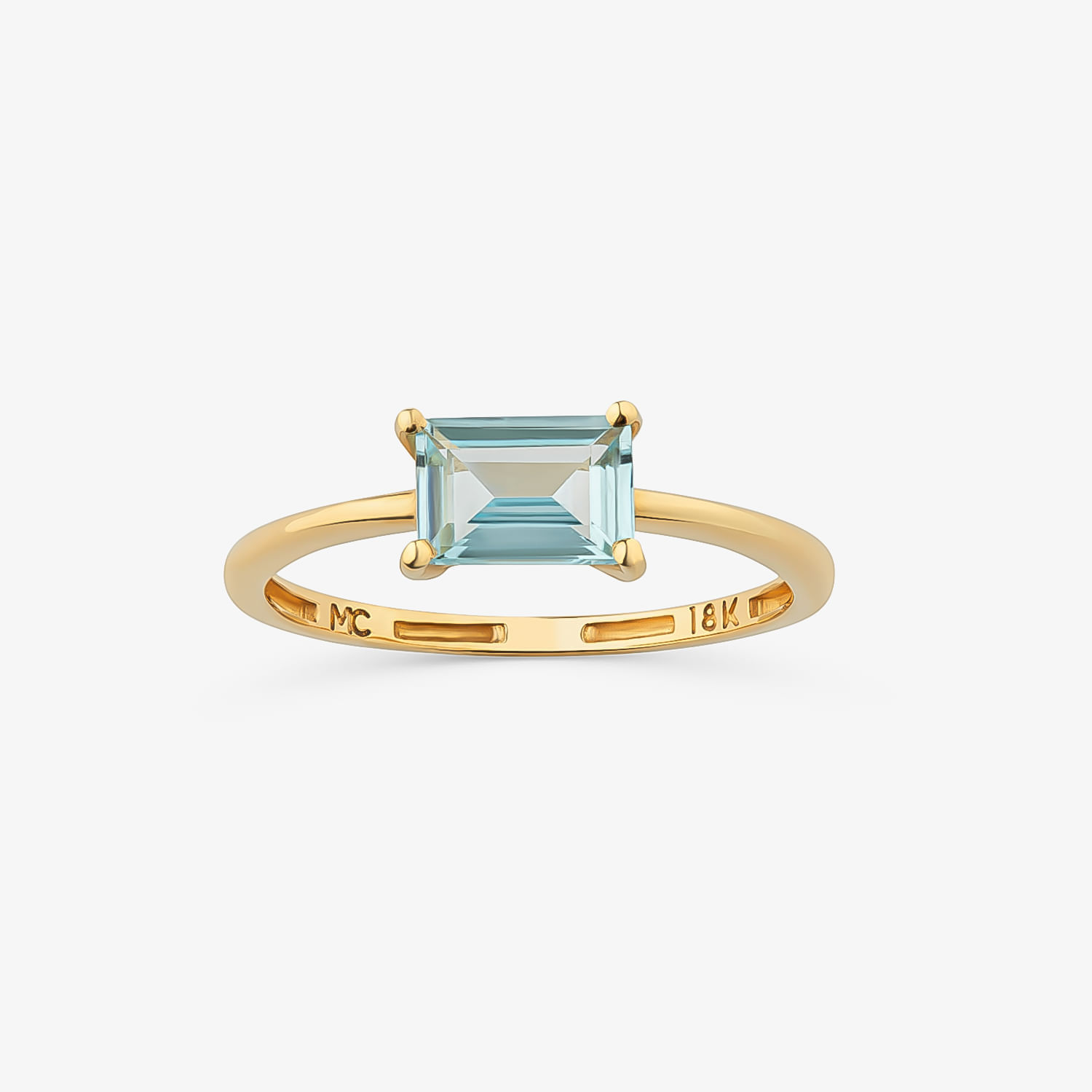 Um elegante anel de ouro com uma grande pedra preciosa azul-clara lapidada em esmeralda, cravejada em quatro garras sobre um fundo branco liso.
