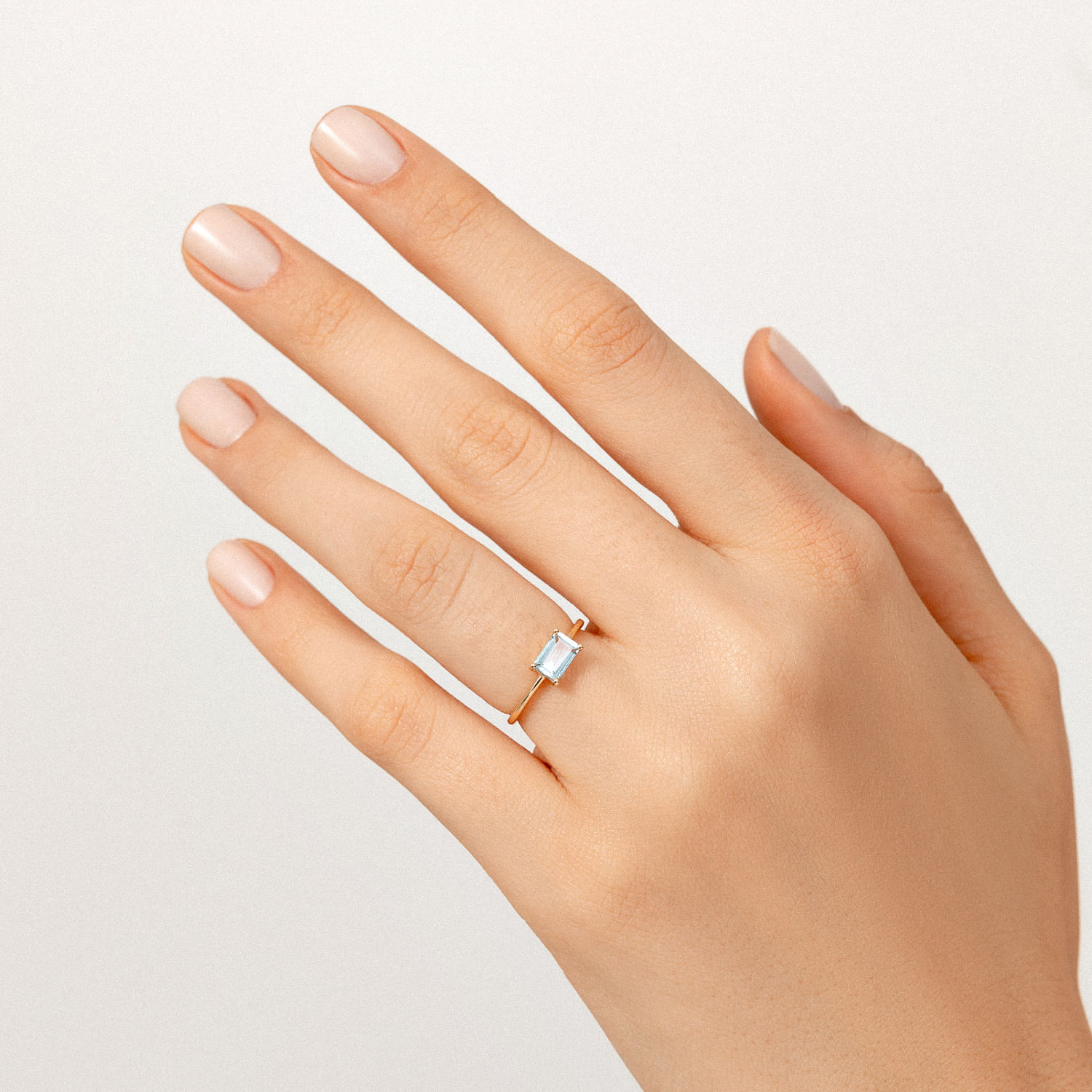 Mão com unhas nude, usando um anel com pedra azul claro em formato retangular.