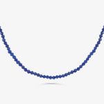 Colar de pedras azuis pequenas, com um efeito de sombra sob a peça, exibido contra fundo branco.