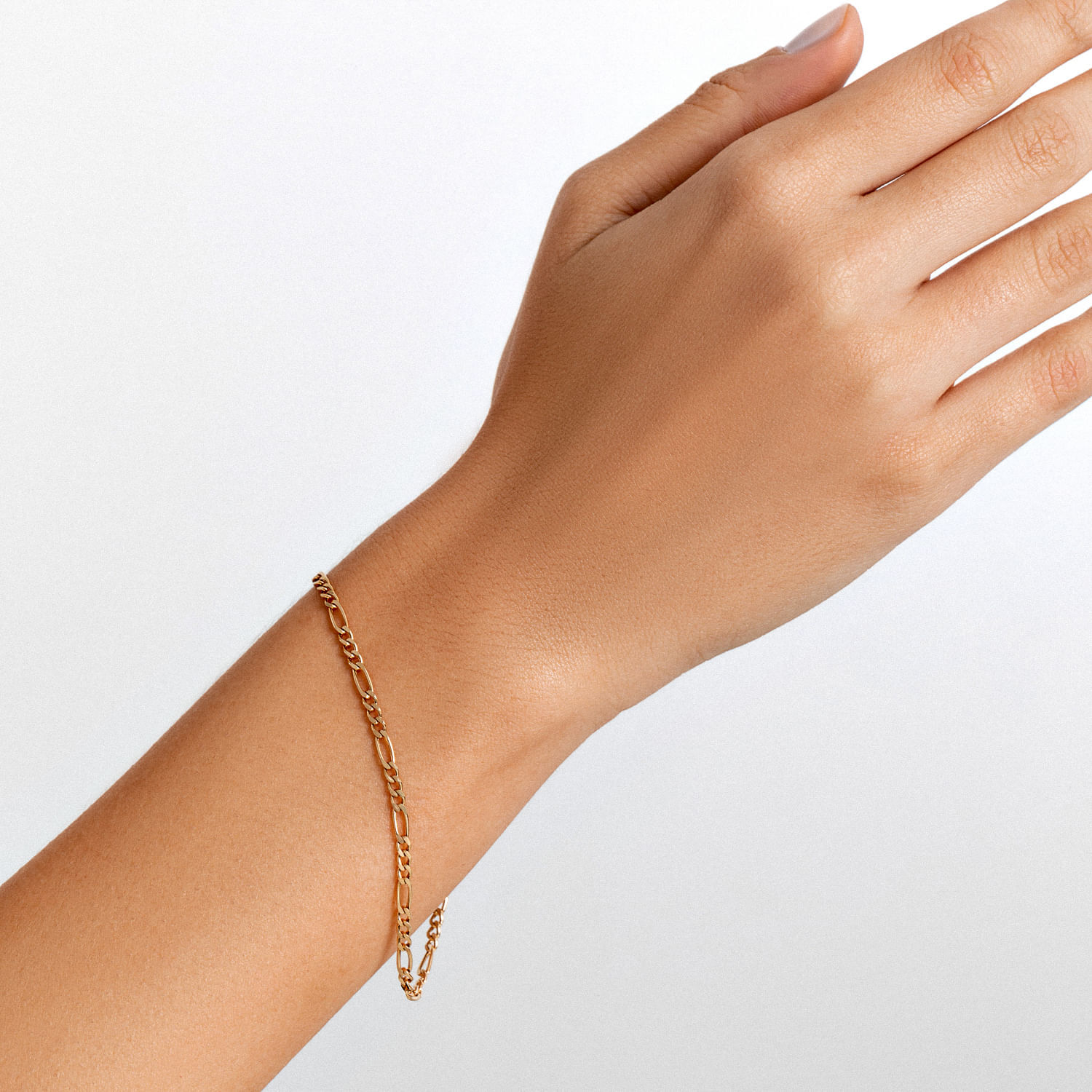 Pulseira dourada com elos finos em volta do pulso de uma mão com pele morena clara contra fundo branco.