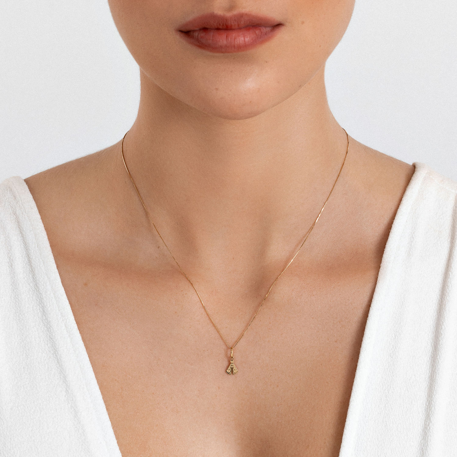 Colar delicado dourado com pingente de lágrima, usado por uma mulher com vestido branco.