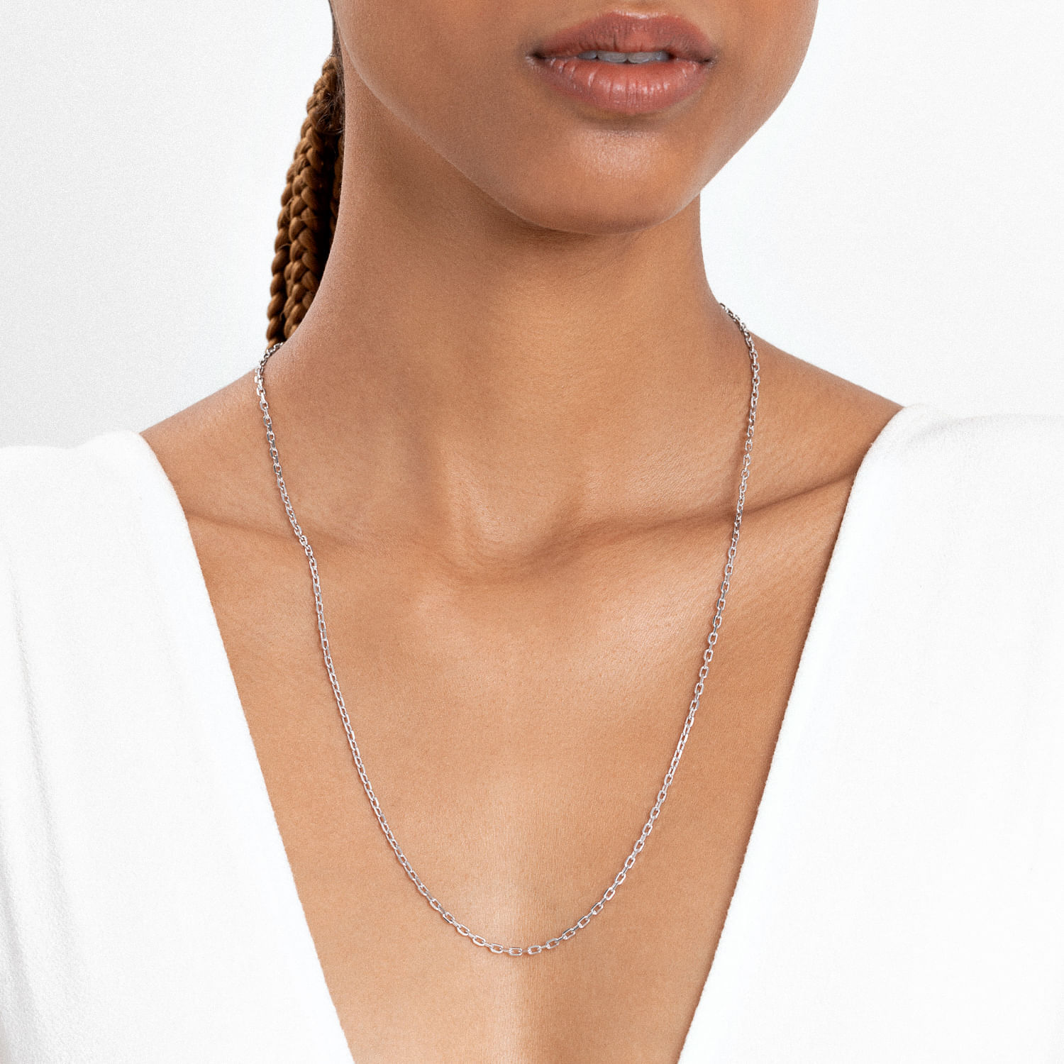 Colar delicado de corrente prateada sendo usado por mulher com pele morena clara, usando roupa branca de decote V.