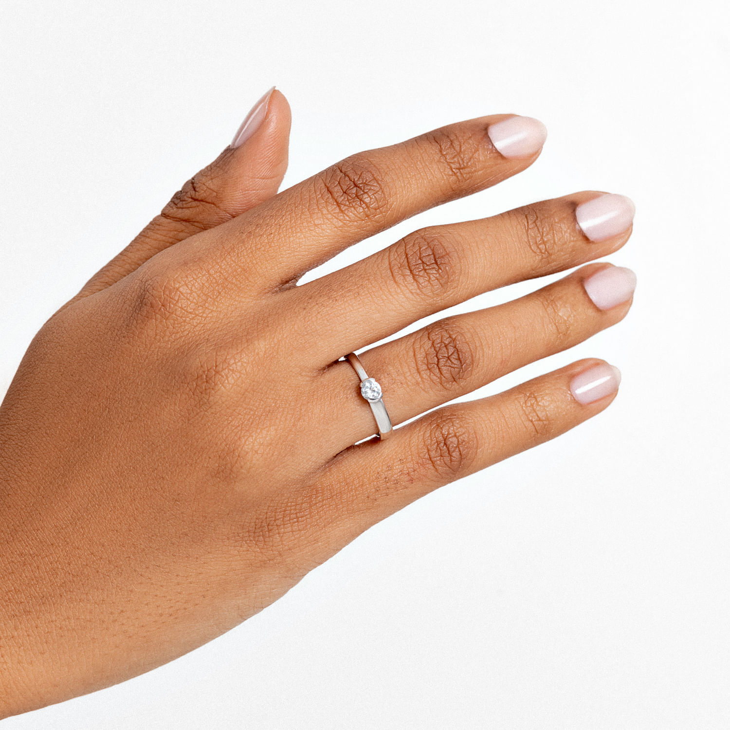 Mão com unha bem cuidada, usando um anel de diamante em um dedo, com fundo branco.