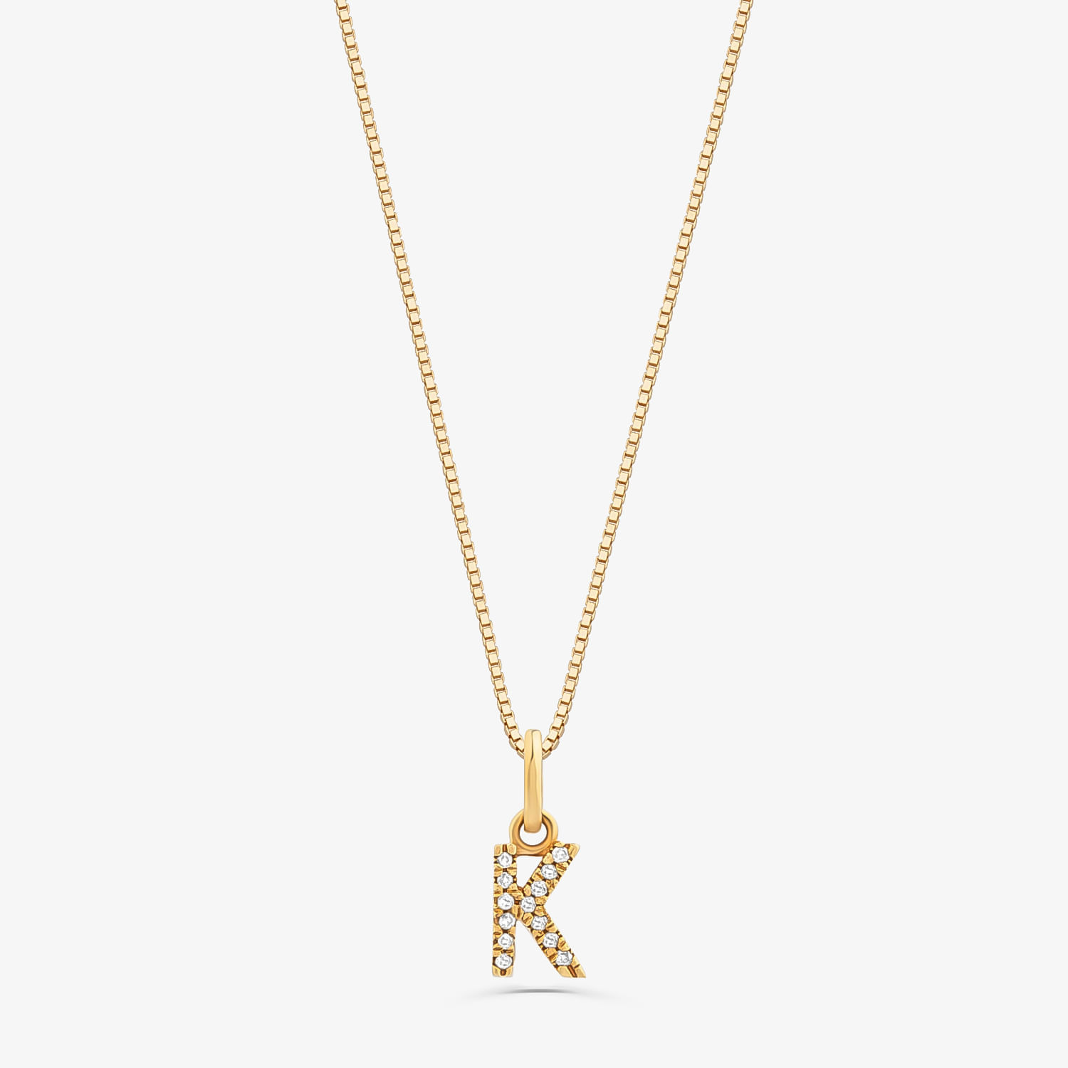 Colar com pingente de letra "K" dourado, decorado com pedras brilhantes, em fundo branco.