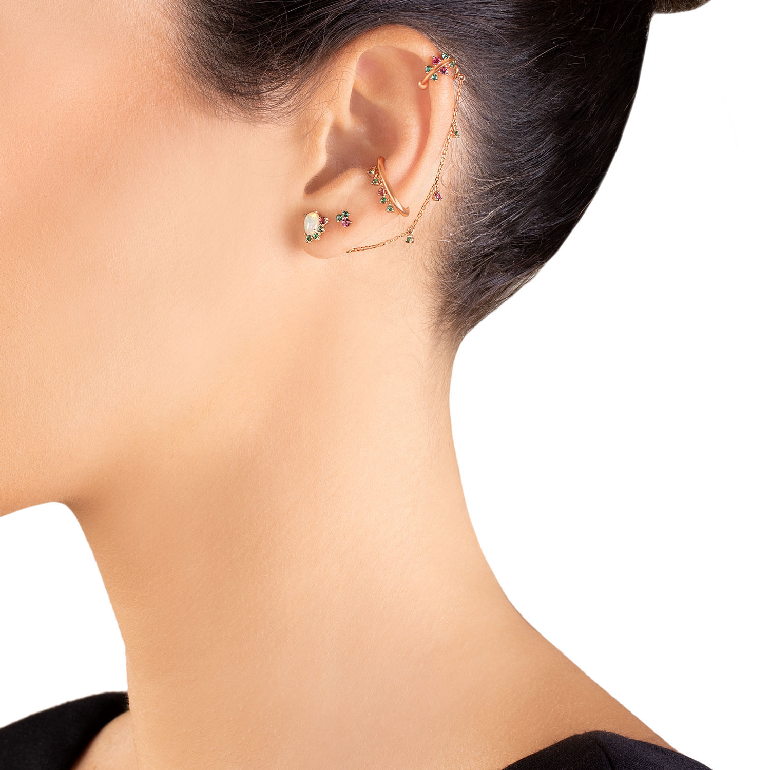 Vários piercings na orelha, incluindo brincos, uma corrente e acessórios multicoloridos, com cabelo escuro e pele clara.
