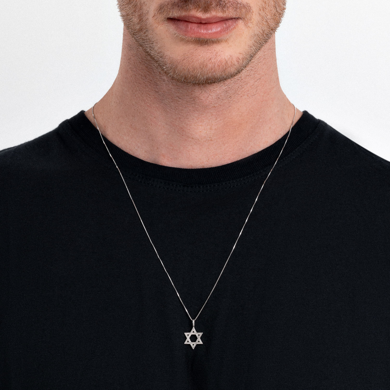 Homem usando uma corrente com pingente de Estrela de Davi, vestindo camiseta preta em fundo branco.
