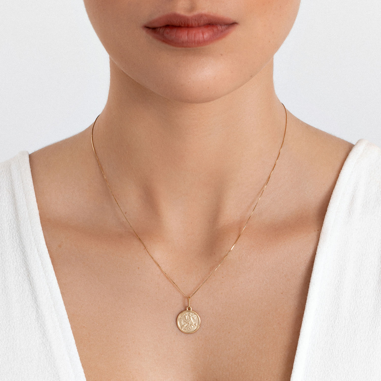 Colar dourado com pingente circular, usado por uma mulher com pele clara e vestido branco.