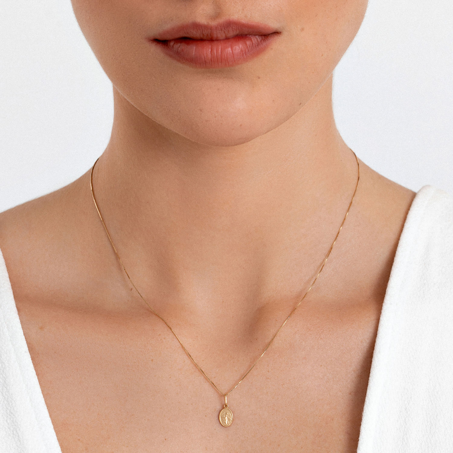Close do pescoço de uma mulher usando uma delicada corrente de ouro com um pequeno pingente oval.