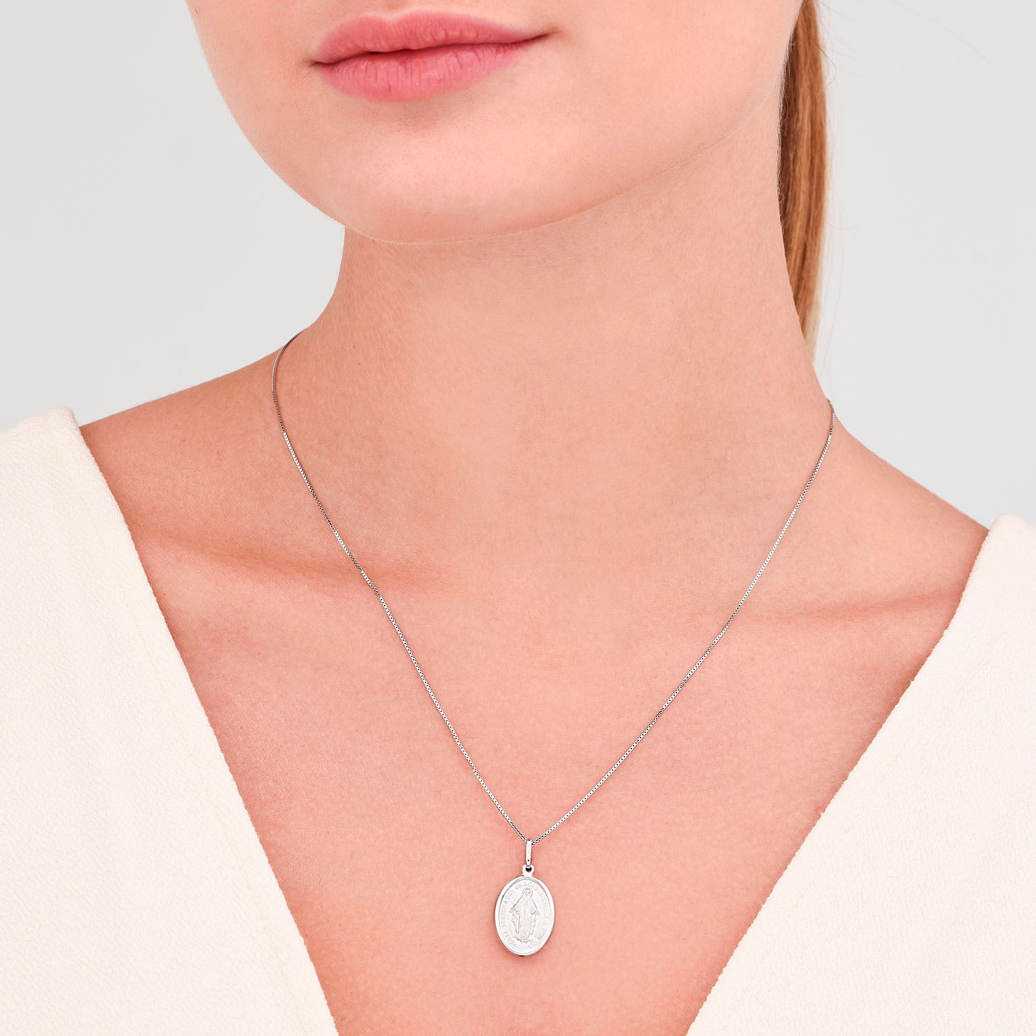 Colar prateado com pingente oval com uma imagem de uma santa ou mãe religiosa.
