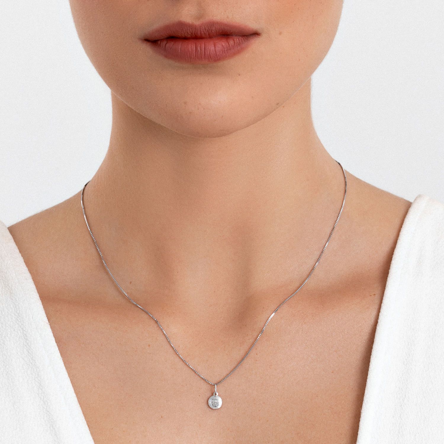 Colar e pingente de prata com pedra brilhante, usado por uma mulher com pele clara e roupa branca.