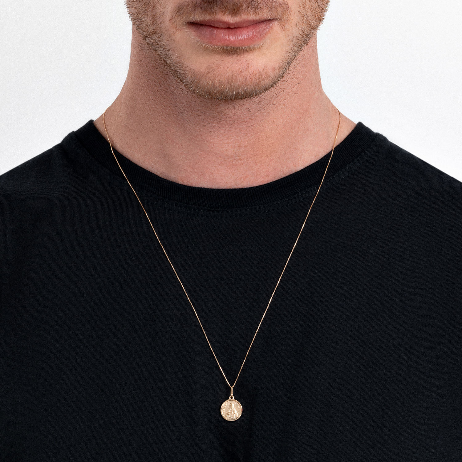 Colar dourado com pingente redondo, usado por um homem com camiseta preta.