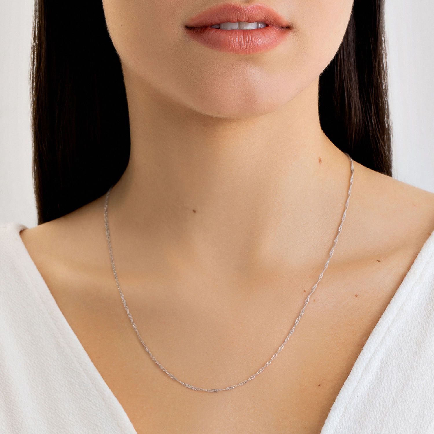 Colar delicado prateado com acabamento texturizado, usado por uma mulher com vestido branco e pele clara.