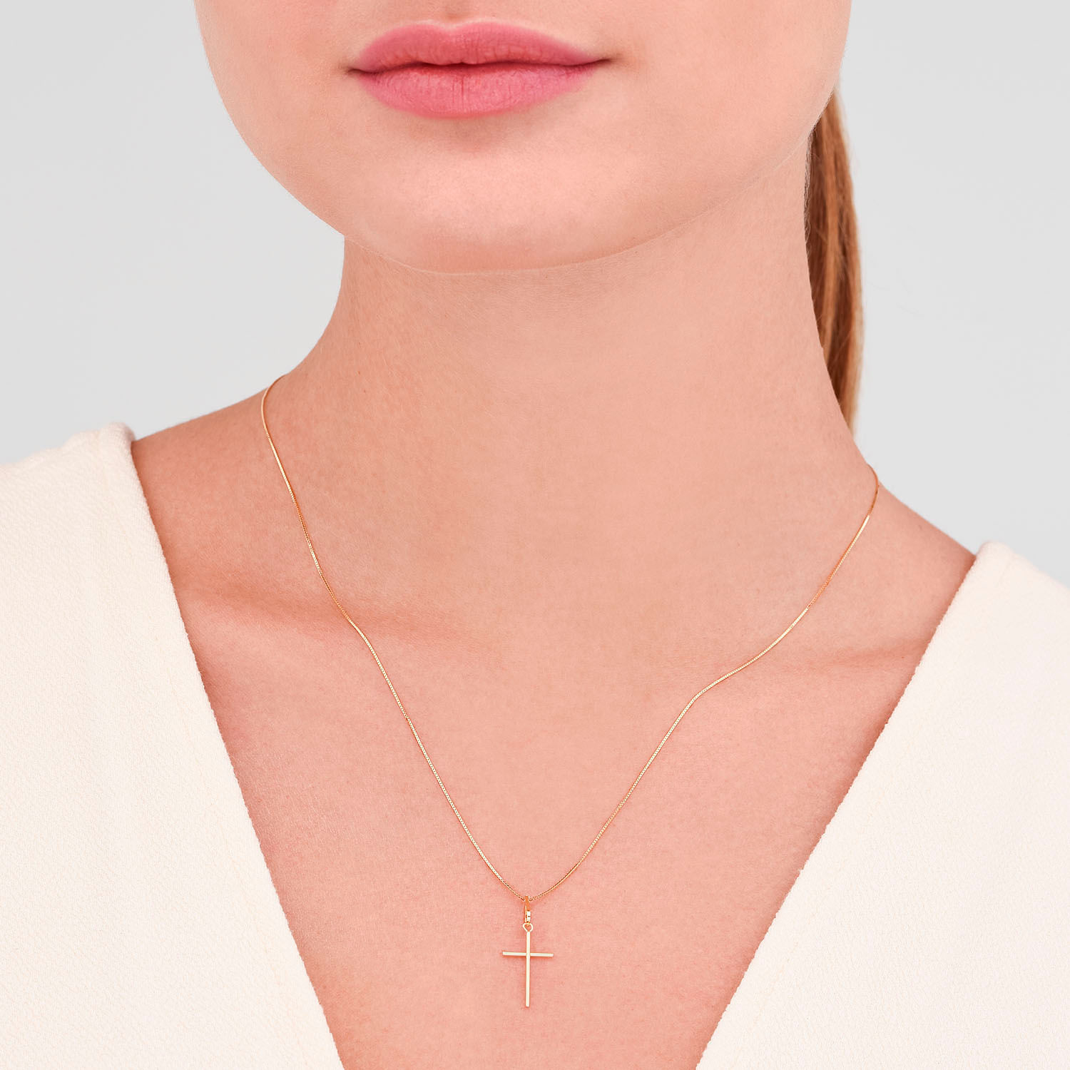 Colar delicado de corrente fina com pingente de cruz dourado, sendo usado por uma pessoa com pele clara e lábios rosados.