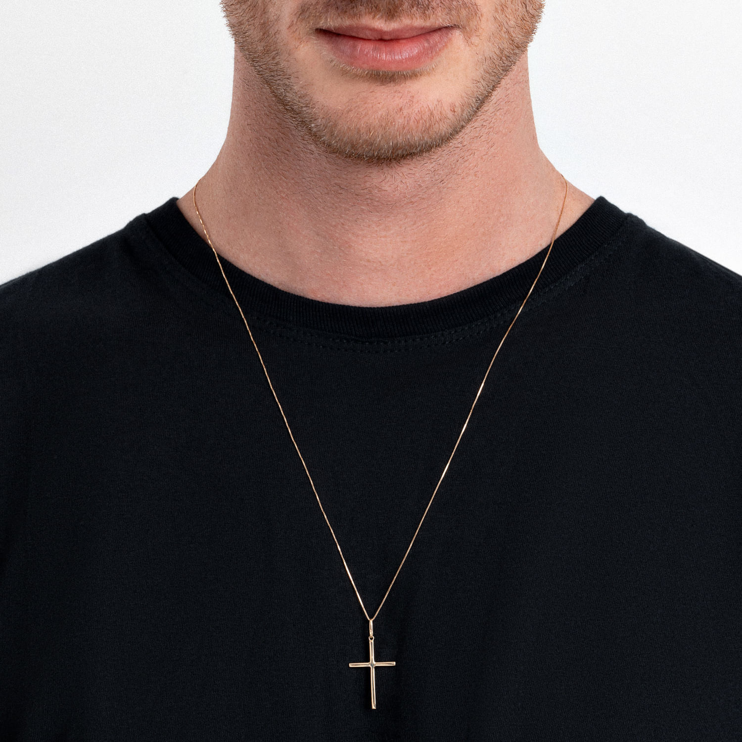 Colar com pingente de cruz, usado por um homem com camiseta preta.