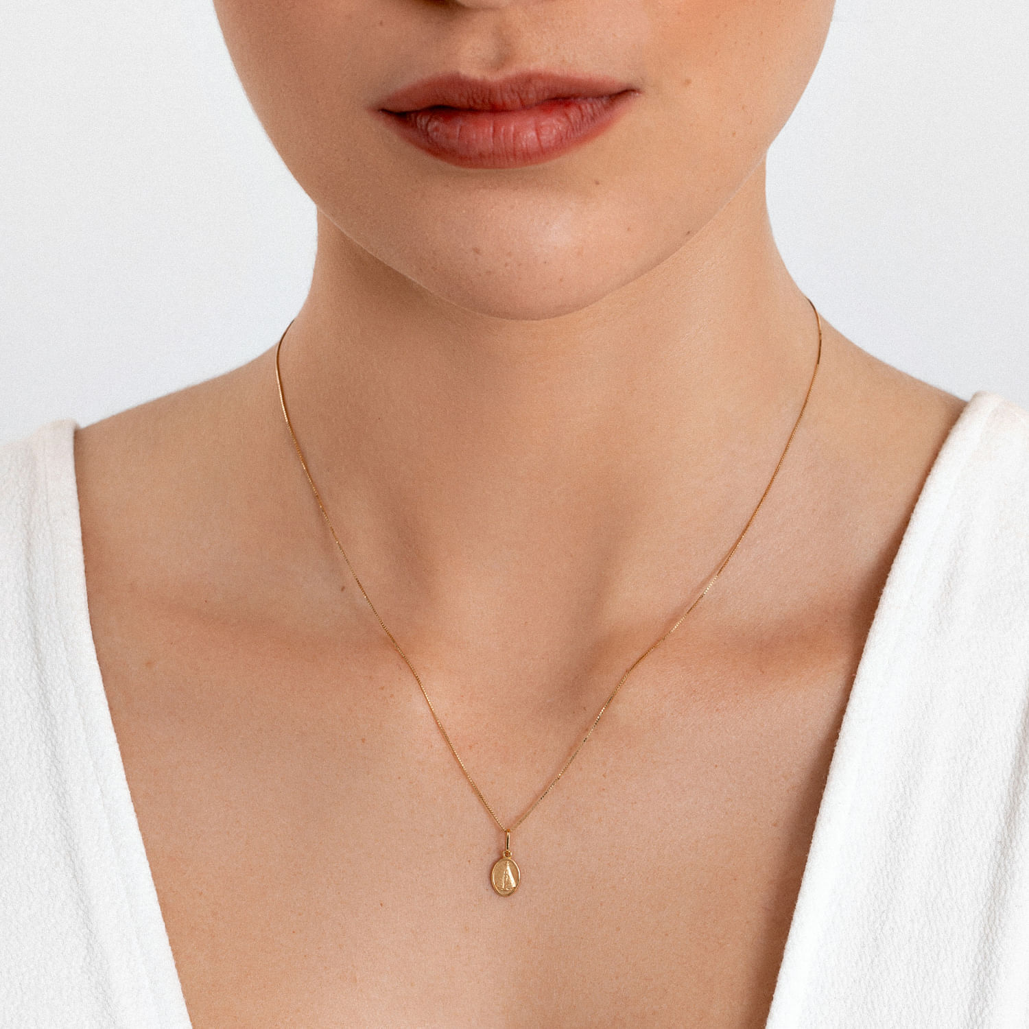 Colar delicado de corrente fina dourada com pingente em forma de gota, usado por uma mulher com camiseta branca.