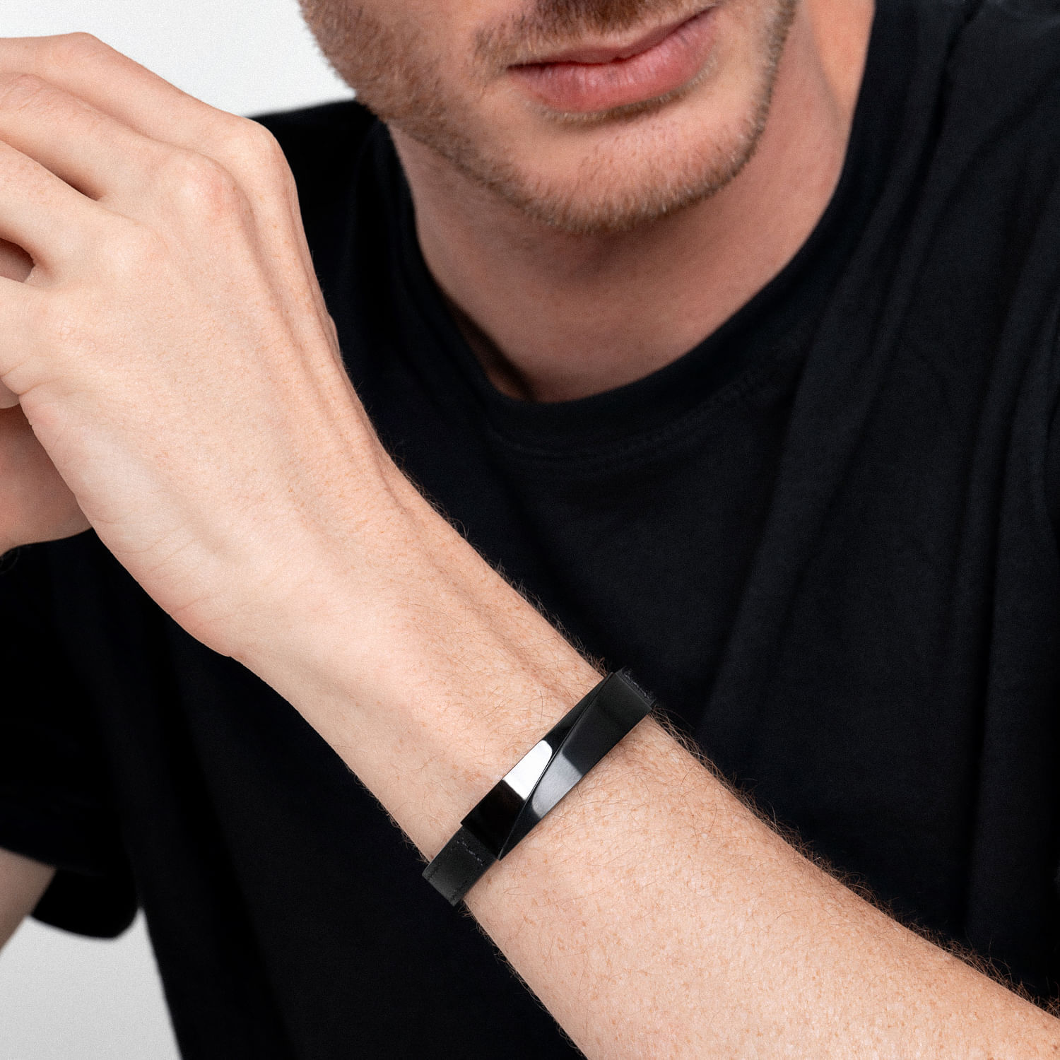 Homem usando pulseira preta de aço no pulso esquerdo, com parte do rosto e mãos visíveis.