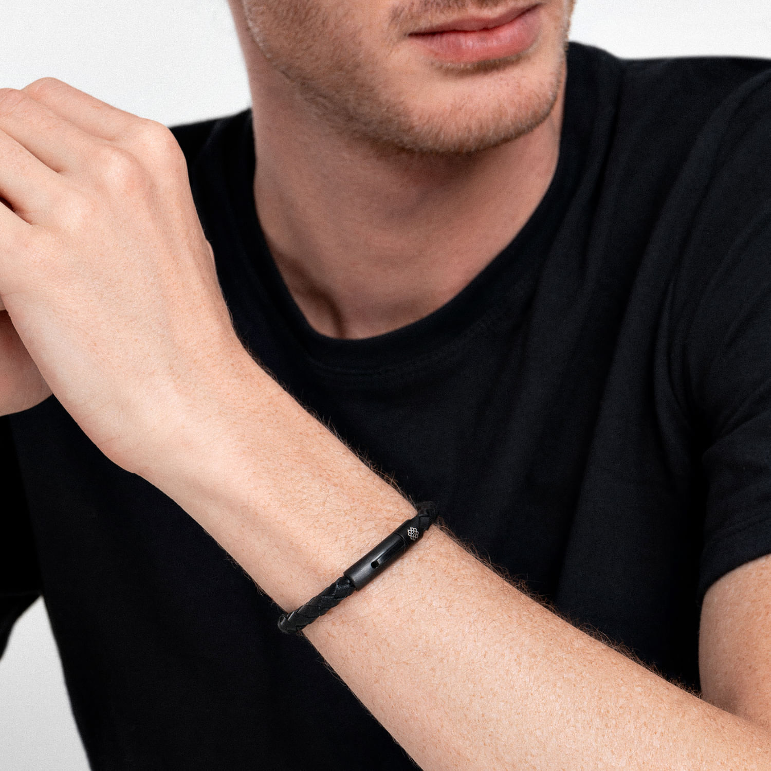 Pulseira preta de corda com fecho metálico acessório no pulso de uma pessoa com camisa preta.