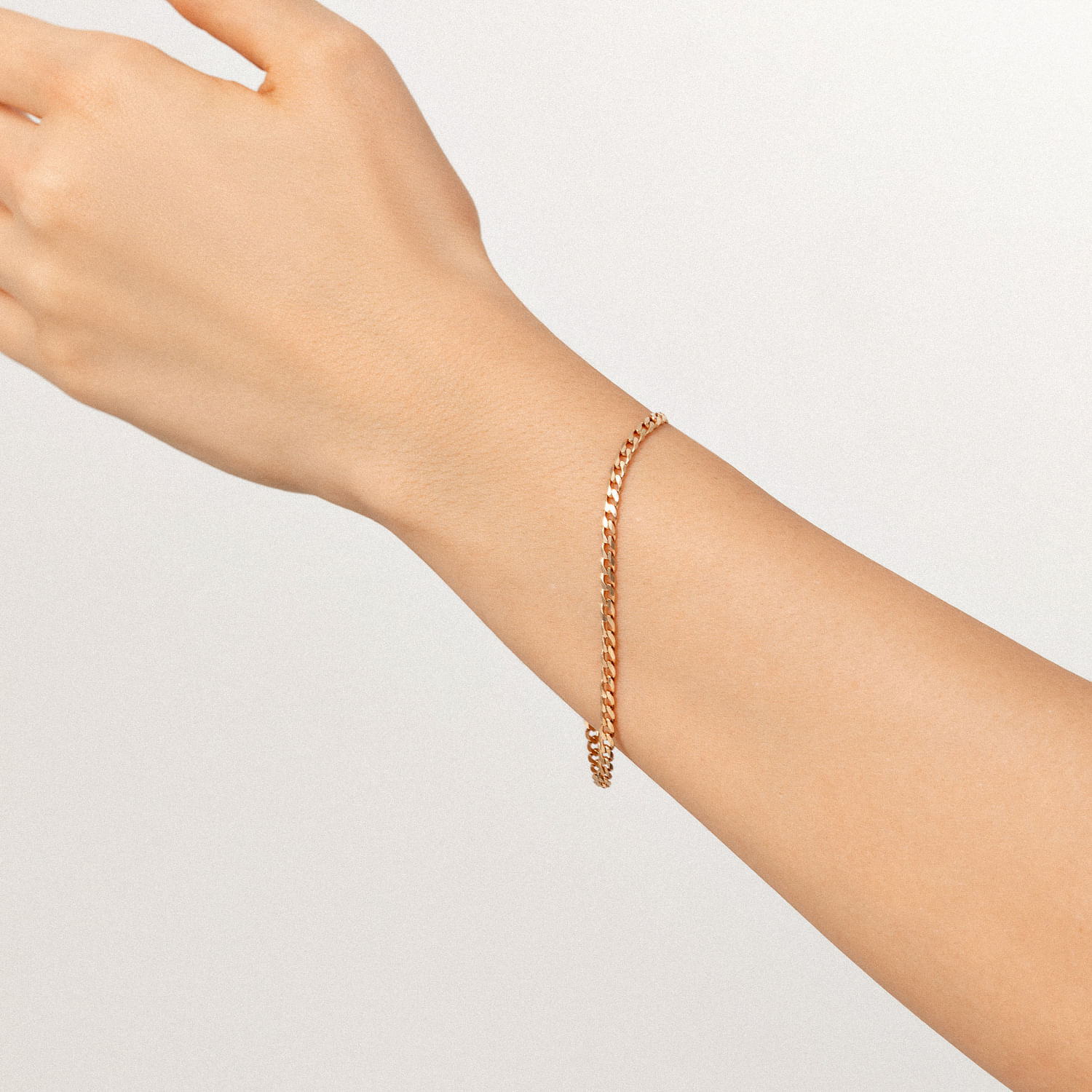 Pulseira dourada de corrente delicada no pulso de uma mão contra fundo branco.