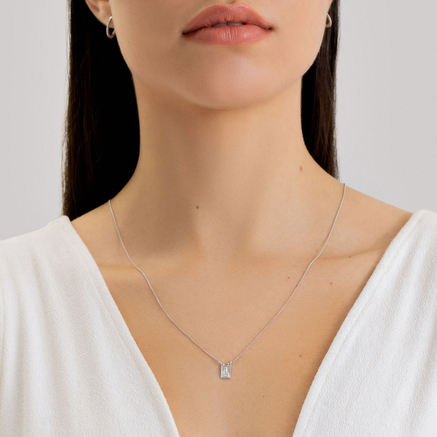 Mulher usando colar delicado com pingente retangular, vestindo blusa branca com decote em V.