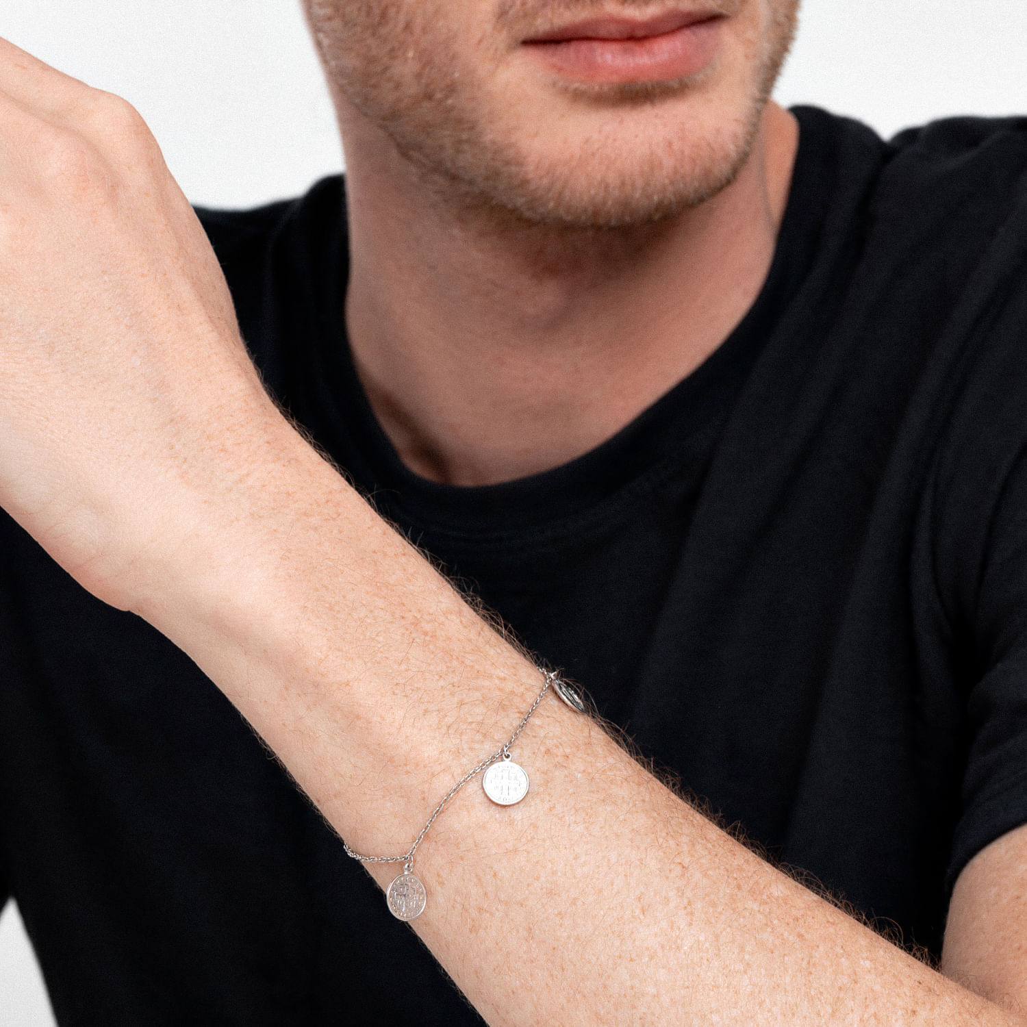 Close-up de um homem vestindo uma camiseta preta e uma pulseira de prata com duas moedas penduradas no pulso.